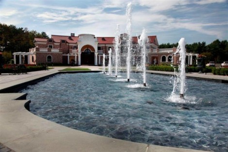 Luxury estate with a stunning water fountain and outdoor furnishings on Long Island. Elegant water fountain with multiple jets in front of a luxurious estate.