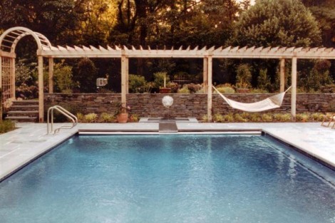 Beautiful Long Island backyard featuring an inground pool, pergola, hammock, and landscaped garden for outdoor relaxation. Inground pool with pergola, hammock, and lush garden in Long Island.
