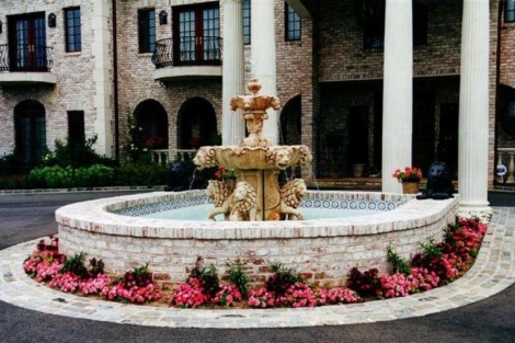 Beautiful stone fountain with lion sculptures surrounded by pink flowers, enhancing outdoor elegance. Decorative stone fountain with lion sculptures and pink flowers in front of a building.
