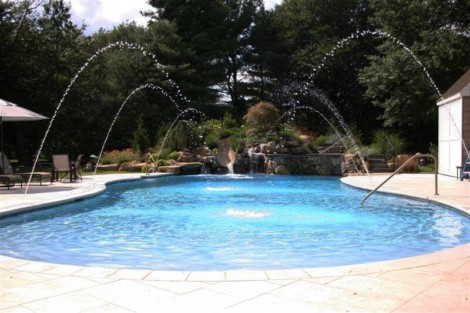 Beautiful inground pool with water fountains and outdoor seating in a landscaped backyard. Inground pool with water features and outdoor furnishings in Long Island.