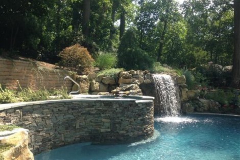 Elegant inground pool with waterfall feature surrounded by lush landscape in Long Island. Beautiful inground pool with waterfall and lush greenery in Long Island.