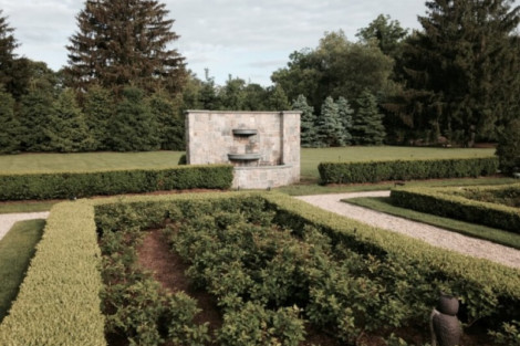A peaceful garden featuring a stone water fountain surrounded by neatly trimmed hedges and lush greenery. Serene garden with a stone water fountain and manicured hedges.