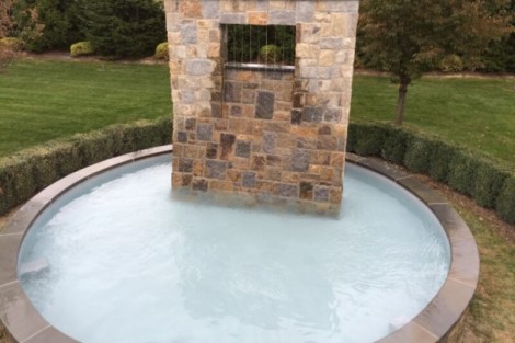 Elegant inground pool with a stone water feature, perfect for outdoor relaxation and entertainment. Inground pool with stone water feature and outdoor landscaping.