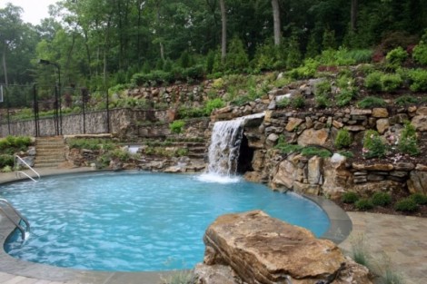 Beautiful inground pool with waterfall feature surrounded by greenery and stonework in Long Island. Inground pool with waterfall and lush landscaping in Long Island.