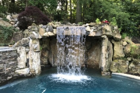 Beautiful stone waterfall feature enhancing outdoor pool area with natural aesthetics. Natural stone waterfall feature for outdoor pools and landscapes.