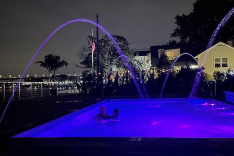 Illuminated inground pool at night with colorful lighting and water features, perfect for outdoor relaxation. Nighttime inground pool illuminated with colorful LED lights and water fountains.