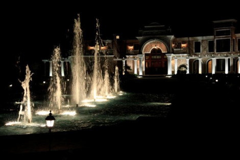 Elegant nighttime fountain with lighting, water jets, and a luxurious building in the background. Night view of illuminated fountain with water jets and grand building backdrop.