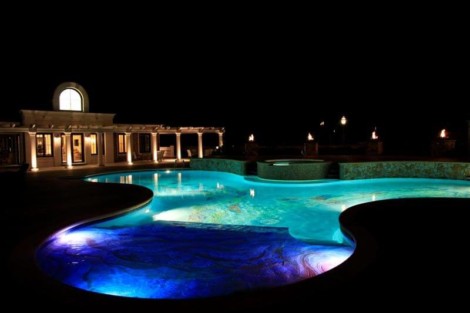 Night view of a beautifully lit inground pool with vibrant underwater lighting and outdoor furnishings. Illuminated inground pool with colorful lighting at night.