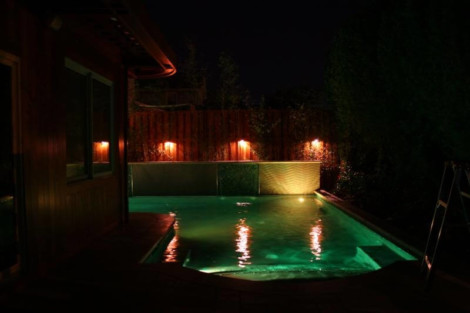 Illuminated inground pool at night with ambient lighting and outdoor setting. Nighttime pool lighting with illuminated water and outdoor ambiance.