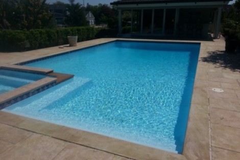 Custom inground pool installed in Long Island with outdoor furnishings and a shaded pavilion. Beautiful inground pool with clear blue water and surrounding patio.