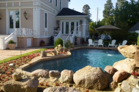 Elegant inground pool with surrounding outdoor furniture and landscaping in Long Island. Beautiful inground pool with natural rock features and outdoor furnishings.