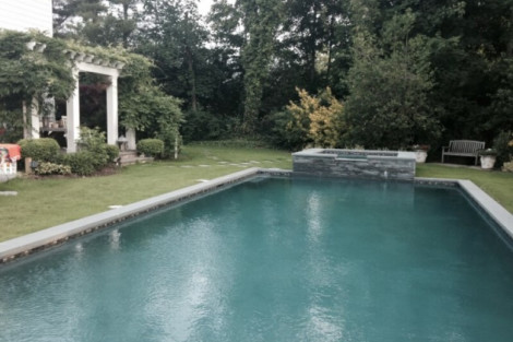 Elegant inground pool with waterfall feature and surrounding outdoor furniture in Long Island backyard. Beautiful inground pool with stone waterfall and outdoor furnishings in Long Island.