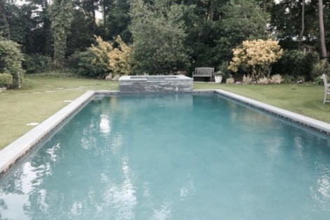Custom inground pool with waterfall and outdoor furnishings in a landscaped backyard. Beautiful inground pool with waterfall feature in a lush backyard.