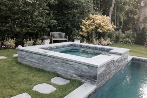 Elegant inground pool with stone finish and outdoor seating area, perfect for outdoor living in Long Island. Beautiful inground pool with stone surround and outdoor seating on Long Island.