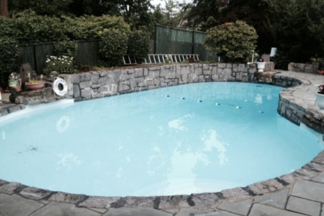 Beautiful inground pool with stone border, outdoor furniture, and lush landscaping in backyard setting. Inground pool with stone border and outdoor furnishings in backyard.