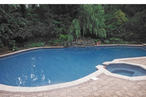 Custom inground pool with hot tub and stone patio, perfect for outdoor relaxation and entertainment. Beautiful inground pool with hot tub and lush greenery backdrop.