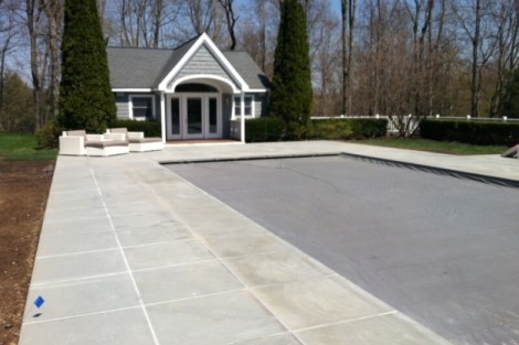 Beautiful inground pool with concrete deck and outdoor seating area in a landscaped backyard. Inground pool with surrounding concrete patio and outdoor furnishings.
