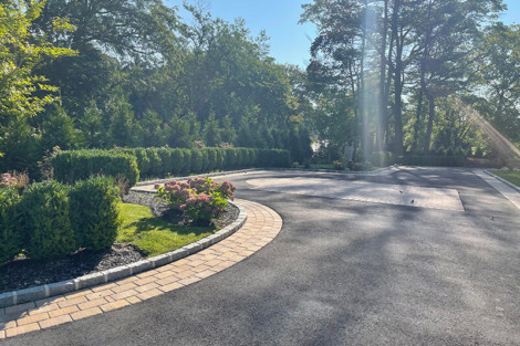 Landscaped driveway with lush greenery and trees, perfect for outdoor living spaces on Long Island. Beautiful paved driveway with landscaping and trees in the background.