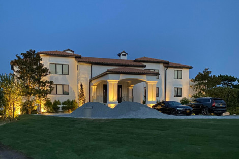 Beautiful luxury home on Long Island with outdoor lighting and a well-maintained lawn. Elegant house illuminated with outdoor lighting at dusk.