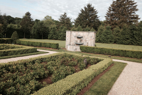 A serene garden featuring a central fountain, neatly trimmed hedges, and tall trees, perfect for outdoor relaxation. Well-maintained garden with fountain, hedges, and trees in the background.