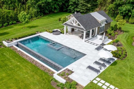 Elegant inground pool with outdoor lounge, cabana, and lush landscaping in Long Island backyard. Luxury inground pool with outdoor lounge area and cabana on Long Island.